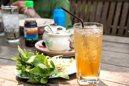 Glass tamarind juice with ice placed on wooden table.Focus top glass,background blur and poor light.の写真素材