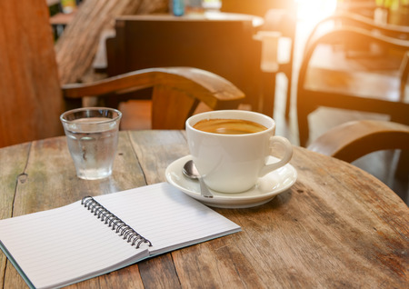 Coffee with notebook and water glass on wooden table.morning lighting.の写真素材