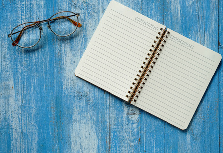 White notebook with glasses on blue wooden floor.の写真素材