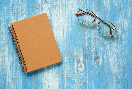 Brown notebook with glasses on blue wooden floor.の写真素材