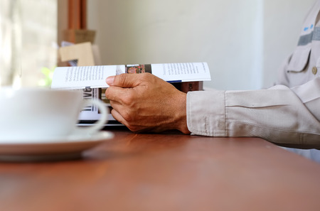 Man reading a book with white coffee cup front place.