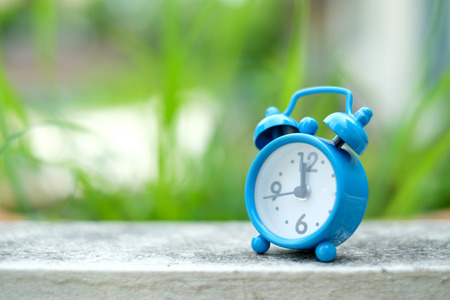 Blue alarm clock on concrete floor with green blurred background.