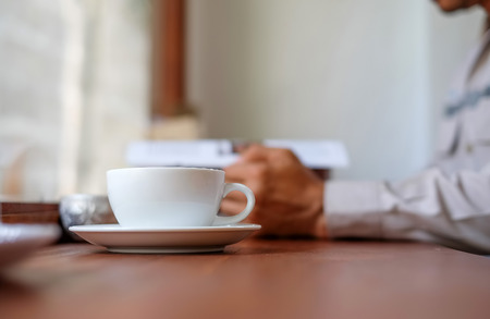 Man reading a book with white coffee cup front place.の写真素材