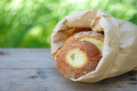 Bread cut pieces in paper bag on wooden table with green blurred background.の写真素材