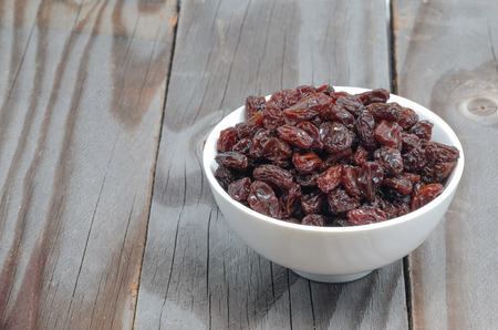 Dried grapes in white cup on wooden floor.の写真素材