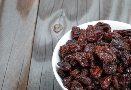 Dried grapes in white cup on wooden floor.の写真素材