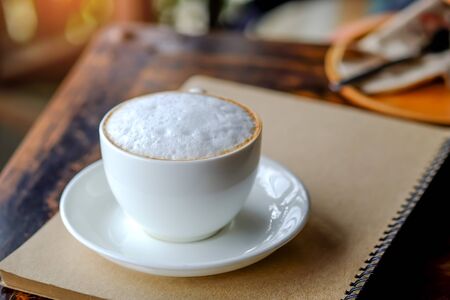 Late coffee white mug place on brown notebook.