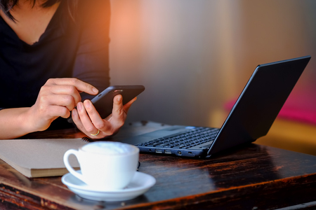 Women working useing smart phone with laptop and coffee on table.の写真素材