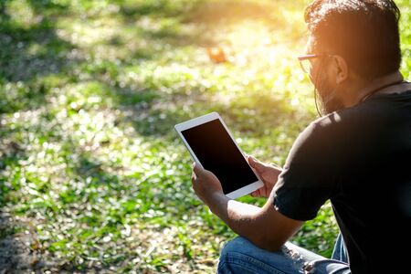 Men sit back playing tablet in the park.の写真素材