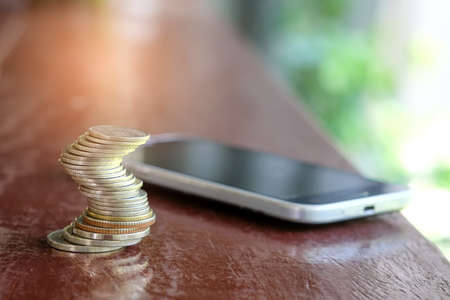Concept Money,Coins with smart phone place on wooden floor.の写真素材