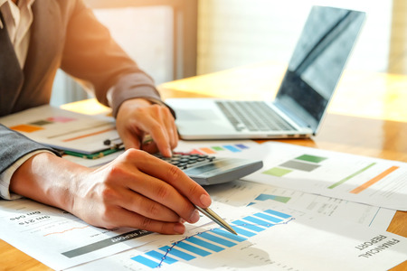 Businessmen are using a calculator and using a pen to analyze data from the graph on the desk.の写真素材