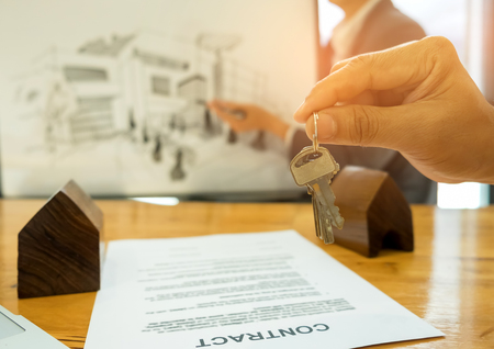 Real estate trading concepts,Close-up House key in hand The back is a house sketch,Modell house and contract documents placed on the table.の写真素材