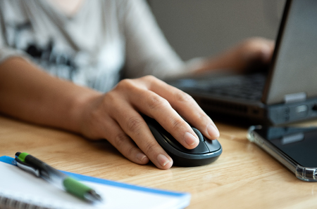Office girl hand are usingmouse to operate laptop.Pen , notebook and smartphone on the desk.