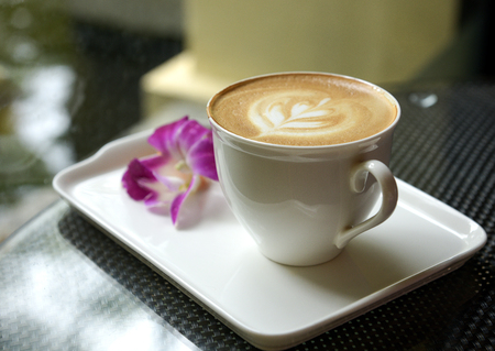 Latte close-up in white mug on Ceramic tray with blurred plumeria flower.の写真素材