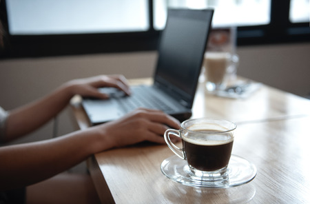 Coffee cup on the front desk with Blurred background hand using laptop.の写真素材