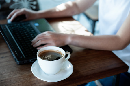Office girl hand on laptop keyboard and mouse.Coffee cup on the table.
