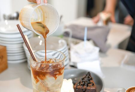 Barista is making mixed coffee. He poured coffee in a glass with ice.