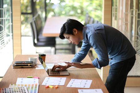Young designer working in an office He bent over to use the laptop and held the tablet in his hand.