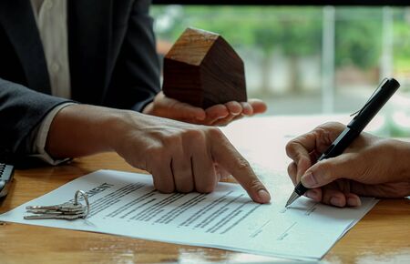 seller hand point the customer to use the pen to sign the contract with house model on seller...