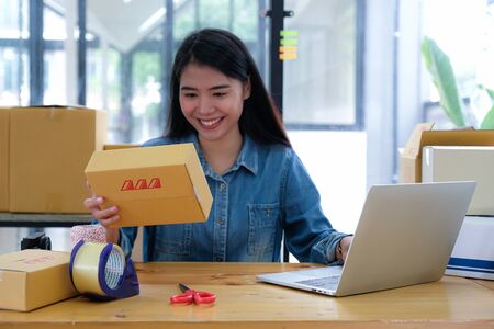 The parcel delivery staff is keying the product number with a laptop. She held the package in her hand and smiled happily at work.の写真素材