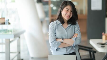 Portrait of a young businesswoman standing with arms crossed and smiling in the office.の写真素材