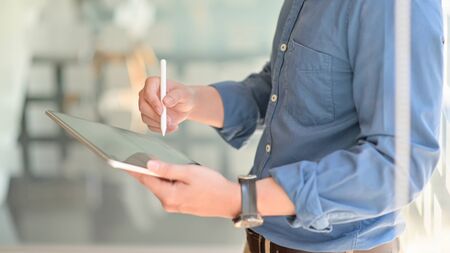 Two young businessmen consulted about their work by using a tablet while standing at working place,...