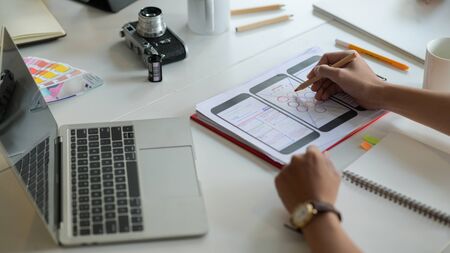 Cropped shot of Designer is sketching a smartphone screen for future customers on the desk with laptop and stationeries.の写真素材