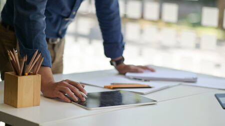 Cropped shot of a Young man holding a pen to use a tablet on the desk with stationery in a...