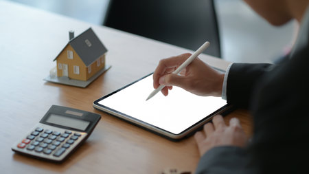Close-up shot of Businesspeople use a pen to write on a tablet with model house and a calculator on the table.の写真素材