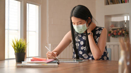 Female insurance agent wearing a mask is introducing a coronavirus health package with a tablet.の写真素材