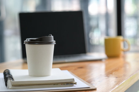 Close-up shot of White take away coffee cup place on a notebook in the office.の写真素材