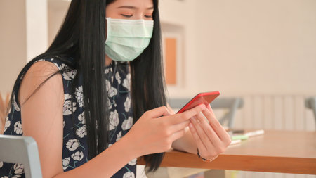 Woman wearing a mask is using a smartphone in a cafe.She is at risk of being infected with the Covid-19 virus.の写真素材