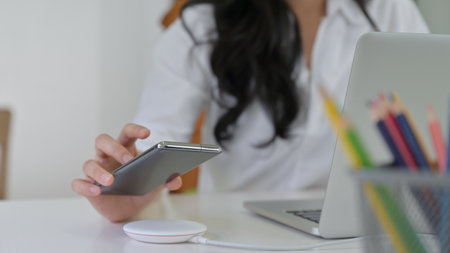 Close-up shot of Girl are putting the smartphone on wireless charger with laptop on the desk.の写真素材