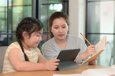 Asian girl studying privately with tutor at home, siblings teaching homework, online learning.の写真素材