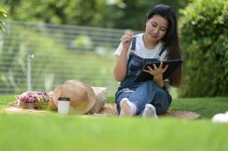 A teenage woman sits in the grass relaxing with a tablet and a cup of coffee, Chatting online.の写真素材