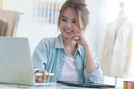 A young woman tailors in a designer's workspace with design equipment, laptop and smartphone in a workshop.の写真素材