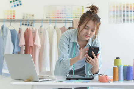 A young woman tailors in a designer's workspace with design equipment, laptop and smartphone in a workshop.の写真素材