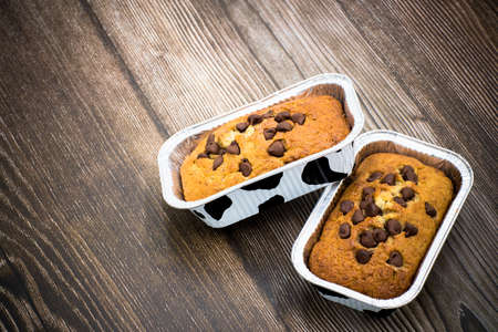 Homemade banana cake on top of semi-sweet chocolate chips in the metal form on wood background.の写真素材