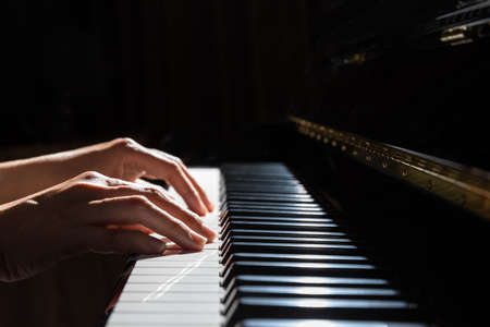 Close-up of a woman hands playing the piano with a dark background.