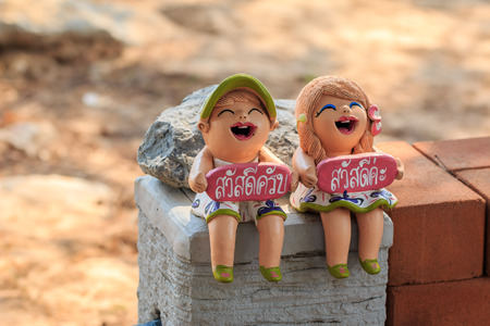 A girl and a boy laughing clay dolls carrying \" Say Hello\" or \" Sawatdee\" label in Thai languageの写真素材