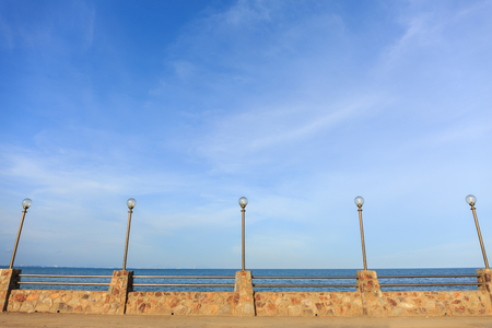 Lamp post and stone fence on road beside blue seaの写真素材