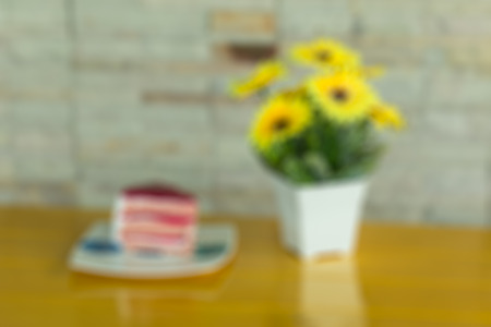 Strawberry layer cake on white dish and   yellow artificial flowers in a white vase rests on yellow...