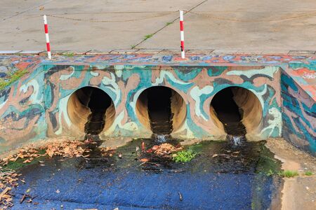 Large cement sewer drain pipe , surrounded by branches and dirt