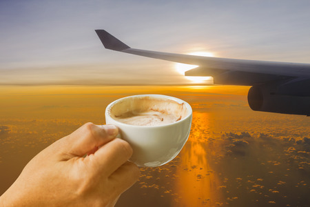 cup of coffee in the hands on Airplane's wing against golden sunlight in early morning backgroundの写真素材