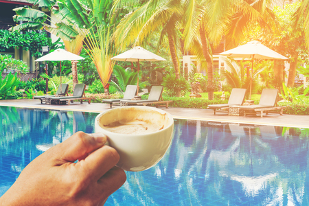 cup of coffee in the hands at Luxurious swimming pool in a tropical garden, Thailand.の写真素材