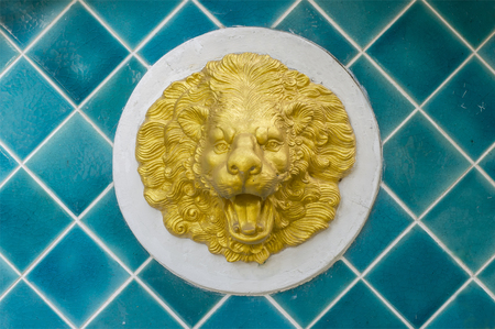 Golden statue of a lion head on a blue tiles wall の写真素材
