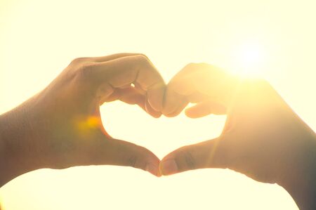 The hands of women and men are the heart shape with the sun light passing through the handsの写真素材