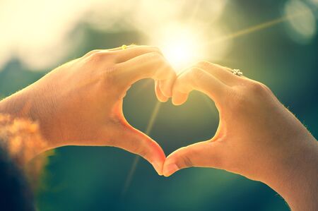 The hands of women and men are the heart shape with the sun light passing through the handsの写真素材
