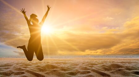 The girl is jumping with fun on the beach, the sea with the golden sun in the evening. summer conceptの写真素材