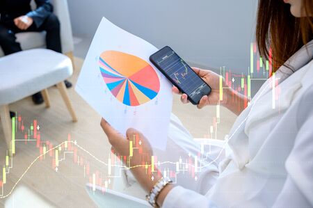Business women wearing white suits are happy to play mobile phones, check the top growth graph of businessの写真素材